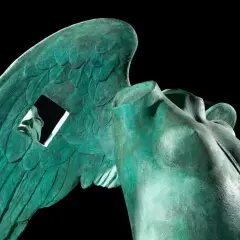 Zielona, miedziana rzeźba anioła z widocznym fragmentem twarzy przez otwór w skrzydle.