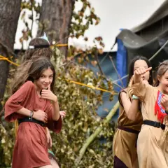 Dziewczynki w strojach indiańskich na scout camp poznań. Jedna pokazuje kciuk w górę, inne pozdrawiają.