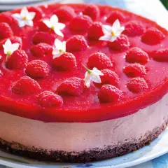 Cheesecake ricetta semplice con lamponi freschi e gelatina rossa, decorata con piccoli fiori bianchi.