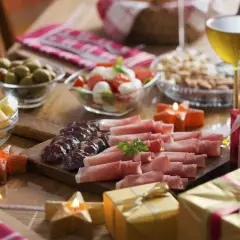 Domowe menu na sylwestra: deska wędlin i serów, oliwki, sałatka caprese, orzechy, wino i prezenty.