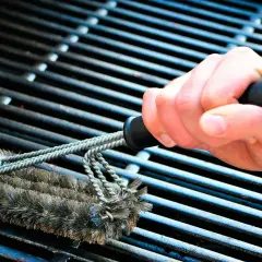 En hand använder en grillborste för att rengöra grillen. Avfettning behövs för att få bort envis smuts.