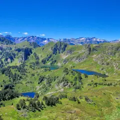 Vue panoramique sur les Pyrénées avec plusieurs étangs bleus, dont l'étang de Rabassoles, nichés dans des vallées verdoyantes sous un ciel bleu intense.