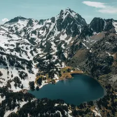 Vue aérienne du lac du Laurenti, niché au pied de montagnes enneigées et de forêts de pins. Un paysage alpin spectaculaire.