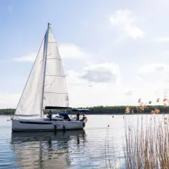 Żaglówka na spokojnym jeziorze, z załogą ćwiczącą różne rodzaje węzłów. W tle las i trzciny.