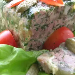 Tranche de pâté de tête maison, garnie de persil, servie sur des feuilles de laitue avec des tomates et des cornichons. Un délice pour une recette de pâté de tête.