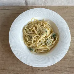 Spaghetti aglio olio z kawałkami sera pleśniowego na białym talerzu.