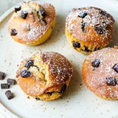 Vier leckere Schoko-Muffins, frisch aus dem Airfryer, mit Puderzucker bestäubt und Schokostückchen.