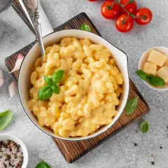 Pyszne, kremowe mac and cheese w białej misce, z bazylią i pomidorkami koktajlowymi. Idealne, gdy zastanawiasz się, jak podgrzać mac and cheese.