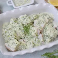 Pyszna ryba w sosie koperkowym, podana w białej misie, z dodatkiem cytryny i świeżego koperku.