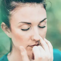 Donna con occhi chiusi esegue esercizi di respirazione, toccandosi il naso con le dita.