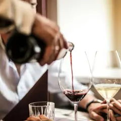 Versando vino rosso in un calice, scoprendo il significato di vino fermo. Accanto, un bicchiere di vino bianco.