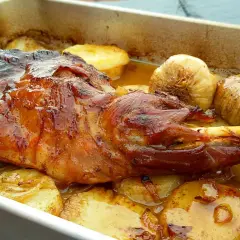 Paletilla de cordero al horno, dorada y jugosa, con patatas y ajos asados. El tiempo y temperatura perfectos para un plato delicioso.