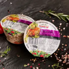 Dwie galaretki drobiowe Szubryt na czarnym tle, otoczone pomidorkami, ziołami i przyprawami. Wartość odżywcza: 233 kJ/55 kcal.