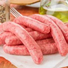Świeża kiełbasa na papierze, obok przyprawy i oliwy. Zastanawiasz się, ile może leżeć kiełbasa w lodówce?