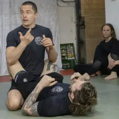 Instruktör visar en teknik i stark bjj. Två kvinnor sitter och observerar.