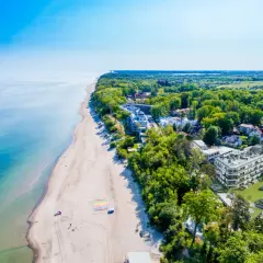 Idealny pobyt nad morzem: piaszczysta plaża, turkusowa woda i nowoczesne apartamenty wśród zieleni.