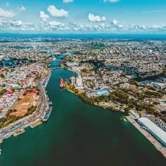 Luftaufnahme der Stadt mit einem Fluss, der sich durch sie schlängelt. Hier ist, wo Santo Domingo liegt, mit Schiffen im Hafen und vielen Gebäuden.