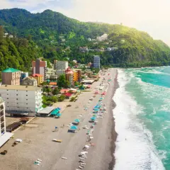Widok na wybrzeże Gruzji, z zielonymi wzgórzami, kolorowymi budynkami i piaszczystą plażą nad turkusowym morzem.