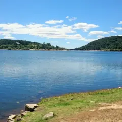 Un día soleado en la ruta del agua La Jarosa, con un embalse azul rodeado de colinas verdes y un cielo con nubes blancas.