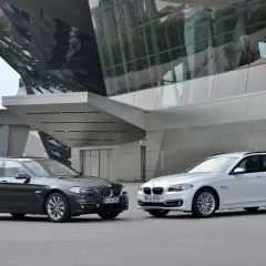 Dwa BMW Serii 5 F10, sedan i kombi, przed nowoczesnym budynkiem. Lata produkcji tego modelu to 2010-2017.