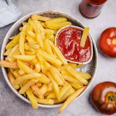 Knusprige Pommes Frites mit einem Schälchen veganem Ketchup. Zwei Tomaten und eine Flasche Ketchup liegen daneben.