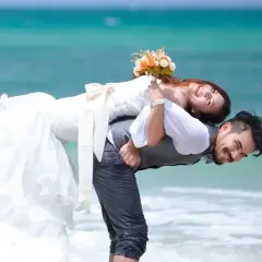 Szczęśliwa para młoda na plaży, co oznacza miesiąc ślubu. Ona na jego plecach, trzyma bukiet.