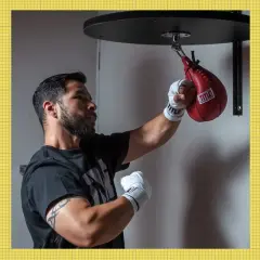 A boxer practices speed bag combos with a red Title bag. An Everlast bag is on the left, and an orange Title bag on the right.