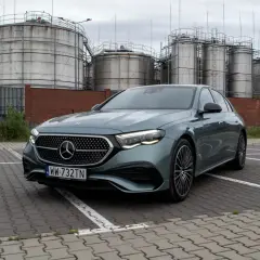 Nowy Mercedes E220d w kolorze zielonym, zaparkowany przed przemysłowymi zbiornikami.