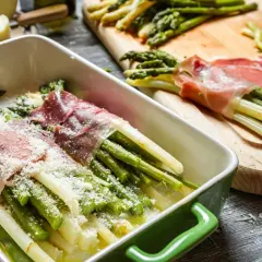 Zielone i białe szparagi w szynce na zimno, posypane parmezanem, gotowe do pieczenia.