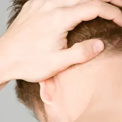 Hand massiert verspannte Muskeln am Hinterkopf.