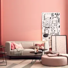 Gemütliches Wohnzimmer mit einer rosa Wand, einem hellen Sofa, Kissen und einem runden Hocker.