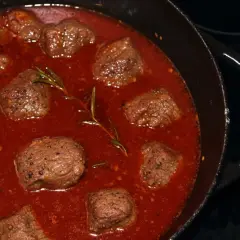 Stracotto di manzo schmort in einer tiefroten Sauce mit Rosmarin. Zarte Fleischstücke, perfekt für ein herzhaftes Gericht.