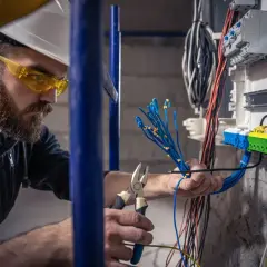 Elektryk w okularach ochronnych i kasku przygotowuje przewody do podłączenia. To dobry przykład, jak zostać elektrykiem.