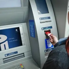 Kobieta wkłada kartę do bankomatu PKO. Ekran wyświetla logo banku i komunikat "Dzień dobry. Proszę, włóż kartę.