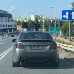 Szare BMW z rejestracją WWL 8830L na drodze, w tle budynki i znaki drogowe.