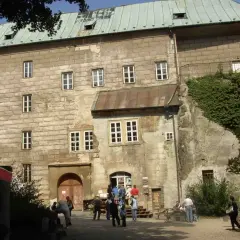 Kamienny zamek Houska z zielonym dachem i licznymi oknami, otoczony zielenią.