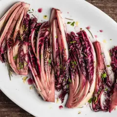 Radicchio al forno, tagliato a spicchi e condito con erbe aromatiche, servito su un piatto bianco.