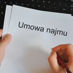 Ręka pisze długopisem umowę najmu. Obok leży kalkulator i klawiatura, gotowe do pracy dla wynajmującego.