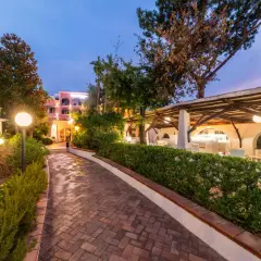 Sentiero in mattoni che porta a un bar all'aperto illuminato, con edifici color pastello sullo sfondo. Un'atmosfera da sogno al Valentino Ischia.