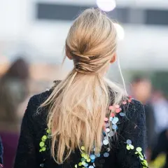 Elegancka fryzura na wesele: blond włosy spięte w niski, luźny warkocz z ozdobnymi pasemkami.