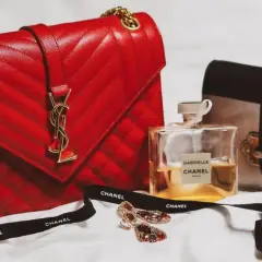 En röd, quiltad modalu väska med gulddetaljer, bredvid en Prada-väska, Chanel-parfym och smycken.