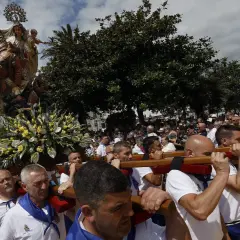 Procesión de la Virgen en las fiestas del Carmen de Foz. Hombres portan la imagen adornada con flores, mientras una multitud observa.