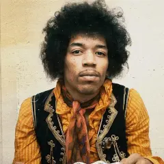 Jimi Hendrix w pomarańczowej koszuli i kamizelce, z charakterystyczną fryzurą. W tle subtelna, lekko zatarte tło, jakby w **purple haze**.