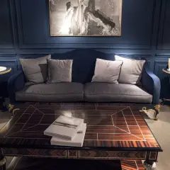 Elegante salón con sofá azul, mesa de centro de madera y dos lámparas de mesa clásicas doradas.
