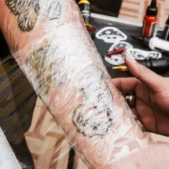 Frische tattoo wunde wird mit Folie geschützt. Tattoo-Farben und Zubehör liegen bereit.