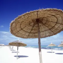 Plaża w Tunezji w grudniu. Słomiane parasole chronią przed słońcem na pustej, piaszczystej plaży.