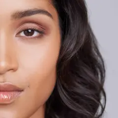Un grain de beauté discret, comme un petit tatouage naturel, orne la joue d'une jeune femme aux yeux expressifs et aux lèvres brillantes.