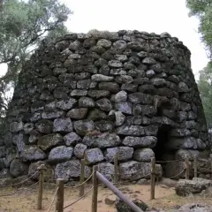 Antico nuraghe di Santa Cristina a Paulilatino, imponente struttura in pietra con un ingresso buio, circondato da alberi secolari.