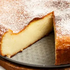 Puszysty sernik z ricotty i mascarpone, oprószony cukrem pudrem, z widocznym kawałkiem ciasta.