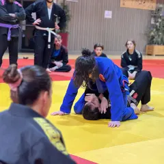 Deux pratiquants de jiu jitsu s'entraînent sur un tapis jaune et rouge. L'un est en position dominante, l'autre en défense.